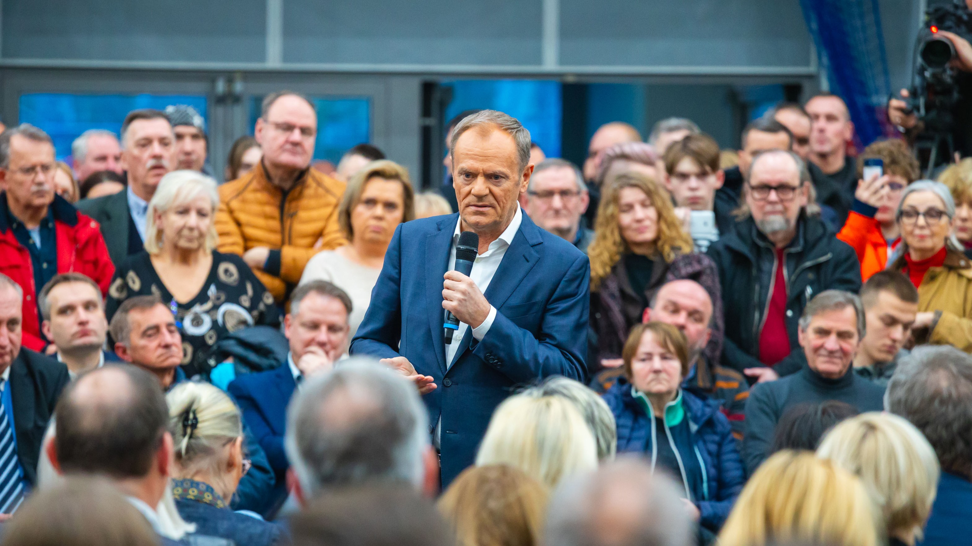 Zdjęcie przedstawia mężczyznę z mikrofonem, który przemawia do publiczności.